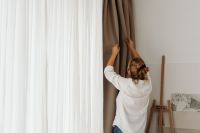 Kaboompics - Woman Pulling Brown Curtains Beside a Window