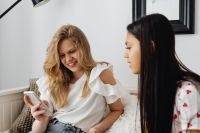 Kaboompics - Close-Up of Teen Friends Sharing Phones While Relaxing on White Bedding