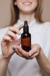 Kaboompics - Beauty Specialist in White Holding Amber Oil Bottle, Clean Skincare Campaign Portrait