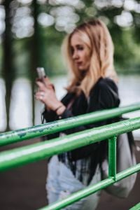 Kaboompics - Blonde woman in a black jacket and ripped jeans by a green handrail