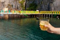 Kaboompics - Yellow Drink Held above the Sea beside a Pier Railing