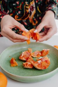 A woman peels an orange on a green plate