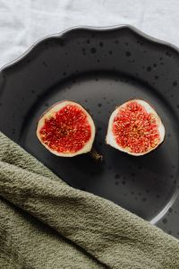 Kaboompics - Two Fig Halves on a Black Stoneware Plate with Green Linen, Dark Food Styling
