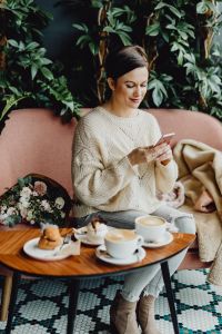 Kaboompics - Woman Checking Her Phone at a Cafe Table with Latte, Pastries and Flowers
