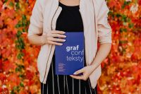 Kaboompics - Woman in a Light Beige Jacket Holding the Blue Grafconf 2017 Book among Autumn Leaves