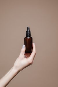 Kaboompics - Small Amber Oil Bottle Held Against Warm Taupe with Copy Space, Natural Skincare Branding
