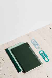 Kaboompics - Green Notebooks and Oversized Blue Paper Clips on Beige Stone, Minimal Study Workspace