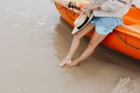 Kaboompics - Barefoot Woman Standing at the Water’s Edge with a Straw Hat Beside an Orange Kayak