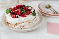 Kaboompics - Side View of Berry-Topped Pavlova with Pink Envelope and Neutral Tableware