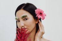 Kaboompics - Asian Woman Portrait with Pink Gerbera in Hair and Red Flower Near Lips