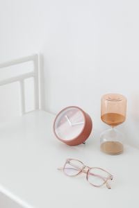 Kaboompics - Pink Table Clock and Amber Hourglass with Rose-Gold Eyeglasses on White Table