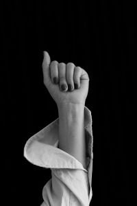 Kaboompics - Raised Hand in White Shirt Sleeve Against Black Background