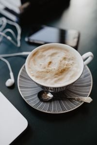 Kaboompics - Cappuccino in a Striped Cup beside Laptop and Earbuds on Dark Desk