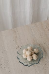 Kaboompics - Small Bowl of Coconut Truffles on Pale Stone, Bright Neutral Dessert Still Life with Curtain Background