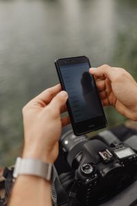 Kaboompics - Hands Checking a Phone above Camera Gear by the Lake