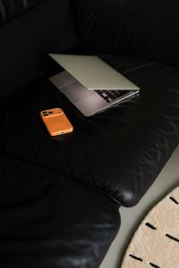 Kaboompics - Laptop and Orange Smartphone on Black Leather Sofa With Copy Space