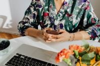 Kaboompics - Woman Using a Smartphone at a Laptop Desk with Blueberries and Flowers