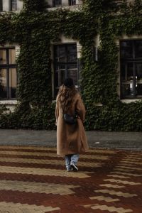 Kaboompics - Woman in Camel Coat Walking Past an Ivy Covered Building