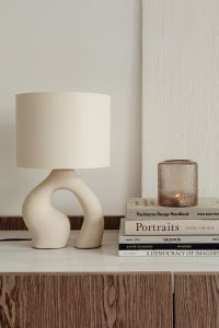 Kaboompics - Sculptural Lamp and Glass Candle Styled with Books on a Wooden Commode