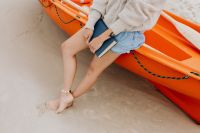 Kaboompics - Close Crop of Woman’s Bare Legs and Book Beside an Orange Kayak on the Beach