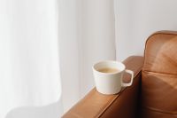 Kaboompics - Sunlit White Coffee Mug on Leather Sofa with Curtain Copy Space for Home Lifestyle Design