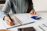 Kaboompics - Asian Woman Writing Notes Beside a Calculator at a Desk