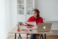 Kaboompics - Woman Looking Through Printed Materials beside Laptop at Home Office Desk