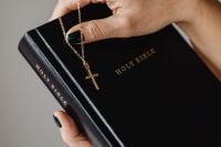 Kaboompics - Hand Holding a Black Holy Bible with a Gold Cross Necklace