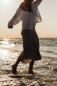 Kaboompics - Faceless Woman Walking Through Sea Foam in White Shirt and Satin Skirt