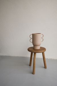 Kaboompics - Wooden Stool with Sculptural Ceramic Mug Against Textured Wall