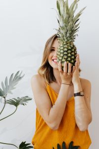 Kaboompics - Playful Close-Up of a Smiling Woman Peeking Around a Pineapple