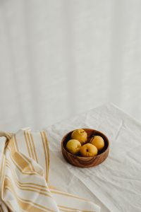 Kaboompics - Japanese Quince in Wooden Bowl on White Linen, Vertical Fruit Still Life with Copy Space