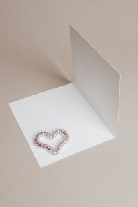 Kaboompics - Pearl Bead Heart on Folded White Card with Beige Background, Valentine's Day Copy Space