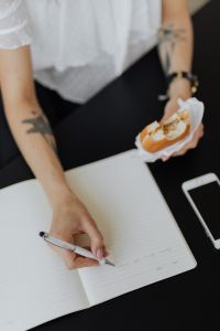 Kaboompics - Freelancer Writing in Notebook While Holding Sandwich
