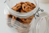 Kaboompics - Open Glass Cookie Jar with Chocolate Chip Cookies and Wooden Lid, Close-Up