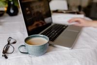 Kaboompics - Coffee Mug and Eyeglasses in the Foreground as a Woman Works on Her Laptop from Bed