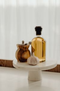 Kaboompics - Vertical Kitchen Background with Olive Oil, Garlic and Wooden Pepper Mill on a White Pedestal Stand, Copy Space