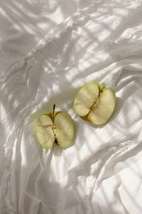Kaboompics - Vertical Still Life of Two Halved Green Apples on White Linen with Soft Window Shadows