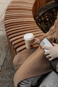 Kaboompics - Close Up of Woman Holding Coffee and Smartphone on a Bench