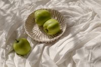 Kaboompics - Two Green Apples in a Fluted Ceramic Plate on Rumpled White Linen, Overhead Still Life