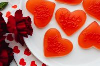 Kaboompics - Orange Heart Gummies and Red Carnations on White Plate