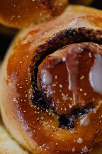 Kaboompics - Single Cinnamon Roll Swirl with White Icing, Vertical Macro Dessert Photography