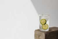 Kaboompics - Tall Glass of Lime Water with Citrus Slices on a Stone Pedestal, Bright Minimal Background with Copy Space