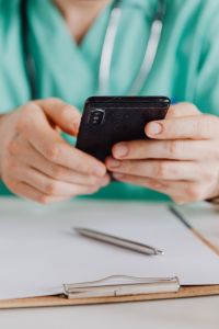 Kaboompics - Doctor Reading Smartphone With Clipboard Nearby