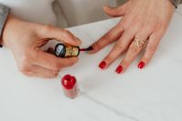 Kaboompics - Red Manicure at Home with Polish Bottle and Hands on a White Marble Countertop
