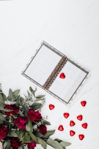 Kaboompics - Open Desktop Calendar with Scattered Red Heart Pralines and Burgundy Bouquet on White Marble