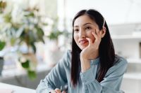 Kaboompics - Smiling Asian Woman Resting Her Hand on Her Cheek at a Desk
