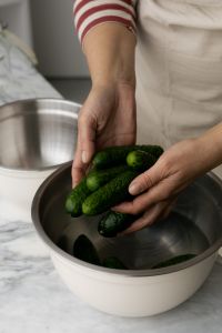 Kaboompics - Hands Holding Fresh Cucumbers over a Stainless Steel Bowl in Kitchen