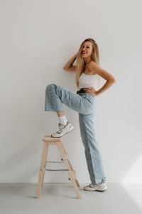 Kaboompics - Smiling Woman Posing in High-Waisted Light Blue Wide-Leg Jeans, Minimal Studio Fashion