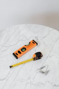 Kaboompics - Spirit Level, Tape Measure and Wall Anchors on a Round White Marble Table, Vertical View